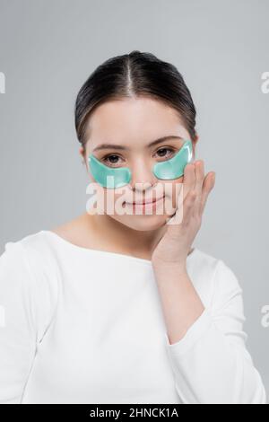 Jeune femme avec le syndrome de Down dans le chemisier appliquant le patch oculaire isolé sur gris Banque D'Images