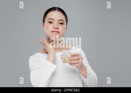 Jeune femme avec le syndrome de Down appliquant le parfum isolé sur gris Banque D'Images