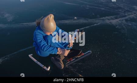 L'enfant s'entraîne sur le patinage de vitesse sur glace. L'athlète met sur des patins. La fille skate en hiver dans les vêtements de sport, lunettes de sport. Patinage de vitesse pour enfants, court long circuit, sport pour enfants. Ralenti extérieur. Banque D'Images