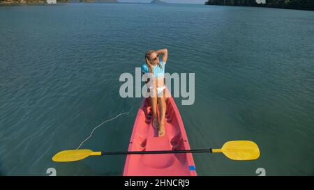 Jolie femme mince en maillot de bain élégant se trouve dans le kayak en plastique rose dérivant sur l'océan azur à la vue supérieure de station exotique. Voyager dans les pays tropicaux. Une fille navigue en kayak dans l'océan, vue au-dessus. Banque D'Images