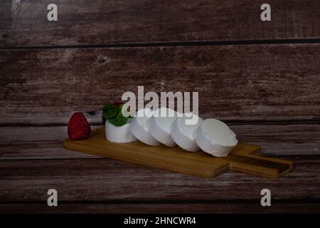 le fromage de chèvre s'enroule avec des framboises et des feuilles vertes sur une planche sur une table en bois Banque D'Images