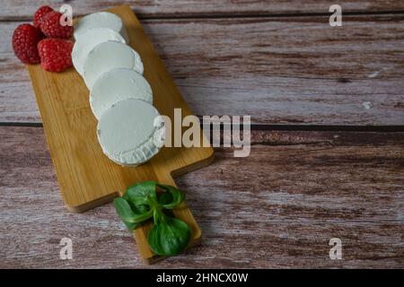 le fromage de chèvre s'enroule avec des framboises et des feuilles vertes sur une planche sur une table en bois Banque D'Images