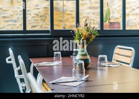 Verres à l'envers servis sur une table avec couverts sur des serviettes et vase coloré avec fleurs fraîches dans un café moderne et clair Banque D'Images
