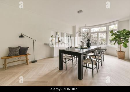 Cette spacieuse chambre lumineuse dispose d''une grande fenêtre et d''une table en bois avec des chaises placées sur un sol en parquet, à proximité d''étagères avec des souvenirs Banque D'Images