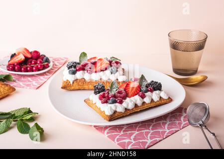 Une savoureuse tarte douce et feuilletée à la crème fouettée et aux baies fraîches est servie sur une assiette près des feuilles de menthe verte Banque D'Images