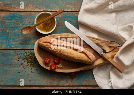 Vue de dessus du pain de baguette fait maison sur une planche à découper en bois avec tomates cerises et couteau sur une table en rade Banque D'Images