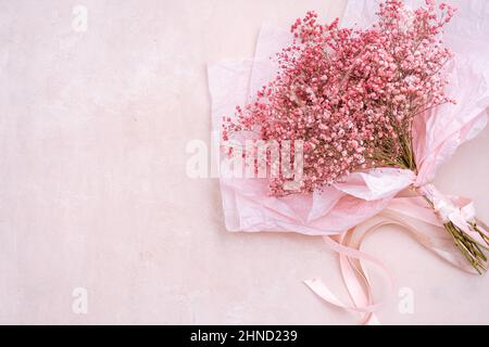 De dessus bouquet de petites fleurs de Gypsophila tendre avec des tiges vertes dans papier d'emballage placé sur fond rose dans la pièce lumineuse Banque D'Images