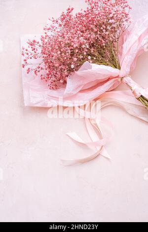 De dessus bouquet de petites fleurs de Gypsophila tendre avec des tiges vertes dans papier d'emballage placé sur fond rose dans la pièce lumineuse Banque D'Images