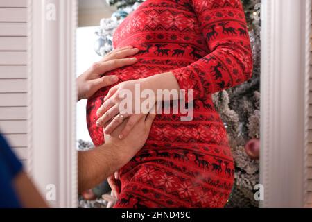 Heureux futurs parents attendent la naissance d'un bébé, le mari se déplace le ventre de sa femme enceinte, reflet de près dans le miroir Banque D'Images