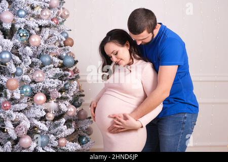 Mari et femme aiment la grossesse ensemble, debout près de l'arbre de Noël. Joyeux Noël et bonne attente pour bébé Banque D'Images