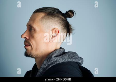 Une photo en gros plan d'un jeune homme dans une veste sur le côté. Un homme aux cheveux longs se rassemblait dans un nœud ou un petit pain d'homme. Sur fond bleu, les coiffures d'hommes, Banque D'Images