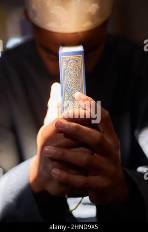 Les mains tiennent le Coran baigné de lumière du soleil à l'intérieur d'une mosquée Banque D'Images