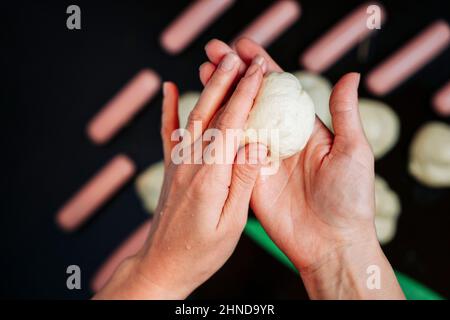 Les mains des femmes sculptent un morceau de pâte pour cuire des saucisses dans la pâte, cuire des hot dogs, les mains des femmes roulent des boules de pâte, table de cuisson Banque D'Images