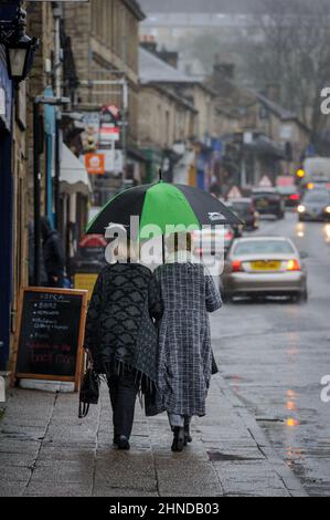 Ramsbottom, Lancashire, Royaume-Uni, mercredi 16 février 2022. Le début de Storm Dudley atteint le nord-ouest de l'Angleterre sur Bridge Street, Ramsbottom, Lancashire. Les Shppers prennent refuge sous un parapluie comme la pluie commence à tomber. Crédit : Paul Heyes/Alay News en direct Banque D'Images