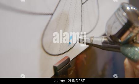 Une artiste apprend à peindre avec un aérographe avec du colorant acrylique, du papier et du chevalet. Intérieur. Concept art moderne, aérographe, aérographie, dessin pulvérisation image créer pulvérisateur dessin graffiti aérosol spray Banque D'Images