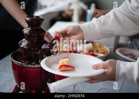 Personne anonyme en trempant des fruits frais sur une brochette dans une fontaine à fondue au chocolat Banque D'Images
