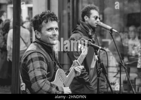 Man joue Godin Multiac Steel Guitar le long d'une rue à York, North Yorkshire, Angleterre, Royaume-Uni, tout en souriant à la caméra. Banque D'Images