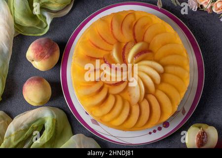 Gâteau de gelée maison avec pêches, crème et biscuit dans une assiette sur fond gris, vue du dessus Banque D'Images