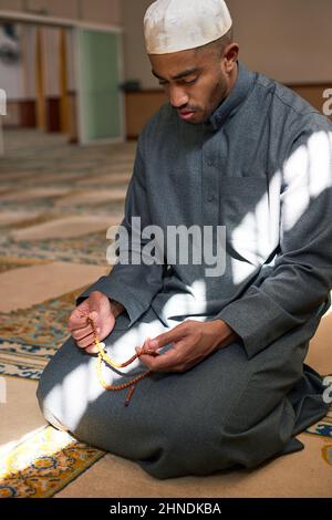 Portrait d'un homme à genoux avec perles de prière dans une mosquée Banque D'Images