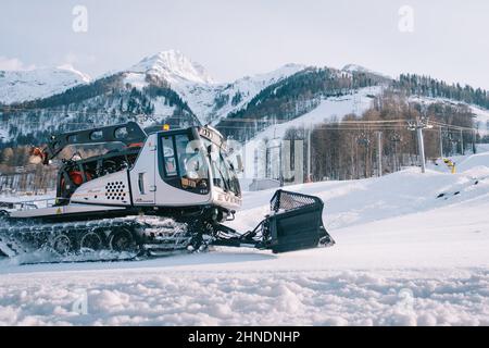 Snowcat 'Prinoth' une grande machine lourde à chenilles en cours de travail préparant les pistes de ski avec des montagnes enneigées en arrière-plan. Banque D'Images