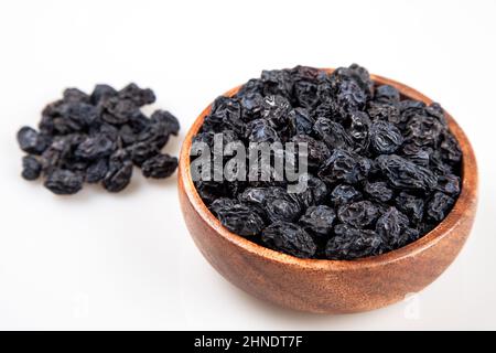 Raisins secs noirs d'un bol complet sur fond blanc Banque D'Images