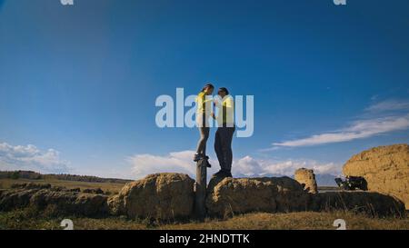 Homme et femme dans le vert jaune sportswear. Couple de voyageurs adorables embrassent et embrassent près de la vieille pierre en profitant du paysage des montagnes. Deux voyageurs se promo dans les montagnes enneigées. Banque D'Images