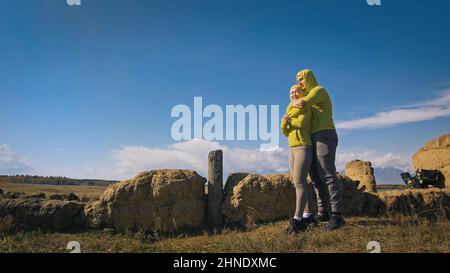 Homme et femme dans le vert jaune sportswear. Couple de voyageurs adorables embrassent et embrassent près de la vieille pierre en profitant du paysage des montagnes. Deux voyageurs se promo dans les montagnes enneigées. Banque D'Images