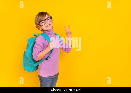 Photo d'un petit garçon doux montrant un v-sign disant bonjour à ses nouveaux amis de l'école isolés sur fond jaune Banque D'Images