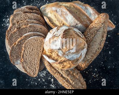 Petits pains frais, pain de blé entier, levain et pain coupé et fariné. Sur fond noir de granit rustique. Espace pour la copie. Vue de dessus Banque D'Images