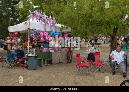 Un homme est assis dans une chaise pliante près d'un stand de vendeur qui vend des jouets gonflables dans la place Santa Fe pendant la Fiesta de Santa Fe 307th au Nouveau-Mexique. Banque D'Images