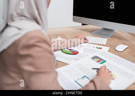 vue partielle d'une femme musulmane floue travaillant avec des infographies et un ordinateur à la maison Banque D'Images