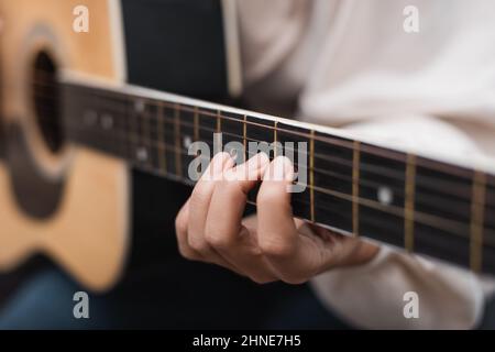 vue partielle d'une femme jouant de la guitare acoustique, arrière-plan flou Banque D'Images