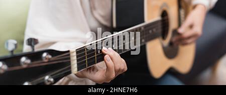 vue partielle d'une femme floue jouant de la guitare à la maison, bannière Banque D'Images