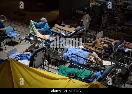 Hong Kong, Chine. 16th févr. 2022. Un professionnel de la santé portant un équipement de protection individuelle (EPI) a vu aider un patient suspecté de Covid-19 sur son lit. Hong Kong a du mal à contenir l'épidémie de Covid-19, la plupart des hôpitaux dépassant leurs capacités. Les patients sur les lits d'hôpital étaient alignés à l'extérieur des services A&E du centre médical Caritas, attendant d'entrer à l'hôpital. Crédit : SOPA Images Limited/Alamy Live News Banque D'Images