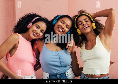 Portrait de trois jeunes femmes portant un casque avec musique contre un mur rose Banque D'Images