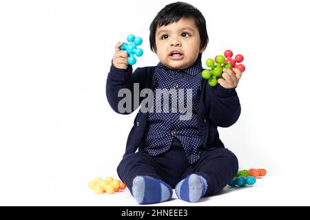 Happy Indian Toddler jouer avec des jouets colorés isolés sur fond blanc. Amusement, activité, éducation, maternelle, anniversaire, Apprentissage, Accueil actif Banque D'Images