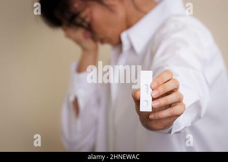 Inquiète déçue femme montrant le dispositif de diagnostic rapide d'antigène Covid-19 avec un résultat de test positif sur la bandelette de test Banque D'Images