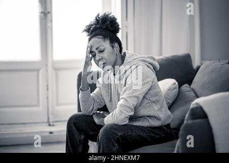 Une jeune femme afro-américaine attractive et dépressive, couchée sur un canapé à la maison, se sentant triste fatiguée et inquiète, souffrant de dépression, de stress et d'anxiété Banque D'Images
