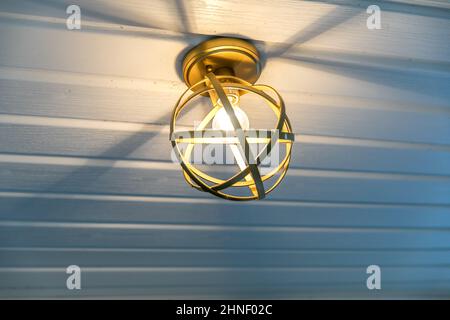 Luminaire d'extérieur rétro doré et chaleureux sur un plafond de véranda Banque D'Images