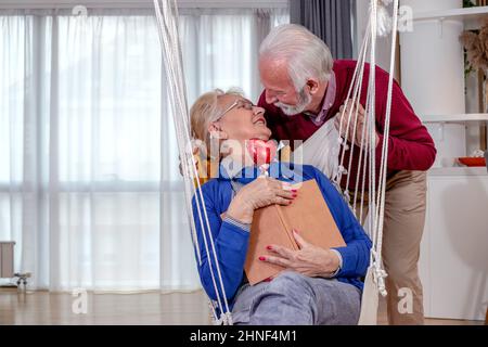 Charmant couple senior dans leur appartement.Le mari surprend sa femme le jour de la Saint-Valentin ou leur anniversaire de mariage avec un coeur. Banque D'Images