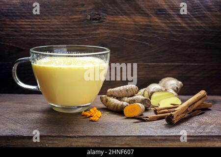 Lait doré au curcuma, gingembre, cannelle et autres épices, boisson ayurvédique saine et boisson détox naturelle tendance sur des planches de bois rustiques sombres, Banque D'Images