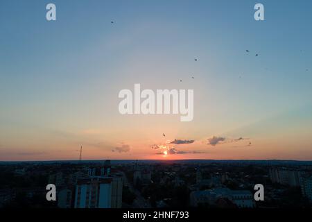 Ciel lumineux et coloré au coucher du soleil avec rayons du soleil et troupeau d'oiseaux volant contre le soleil couchant. Banque D'Images