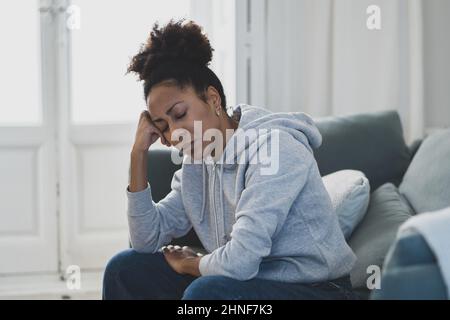 Une jeune femme afro-américaine attractive et dépressive, couchée sur un canapé à la maison, se sentant triste fatiguée et inquiète, souffrant de dépression, de stress et d'anxiété Banque D'Images