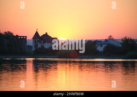 Silhouette sombre de maisons de banlieue devant l'eau du lac au coucher du soleil. Banque D'Images