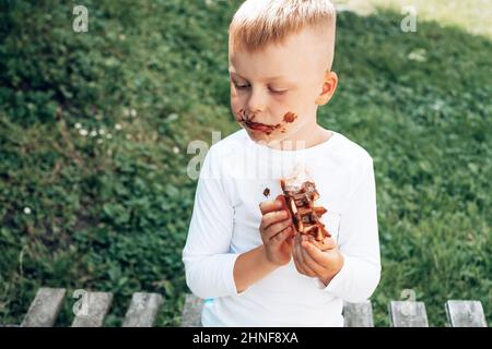 L'enfant mange une gaufre belge avec une garniture au chocolat. Vue de dessus. La vie quotidienne sale tache pour le lavage et concept propre Banque D'Images