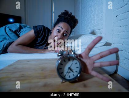 Sans sommeil et désespéré belle afro-américaine éveillé la nuit ne peut pas dormir regardant l'horloge souffrant d'insomnie dans le désordre de sommeil et Banque D'Images