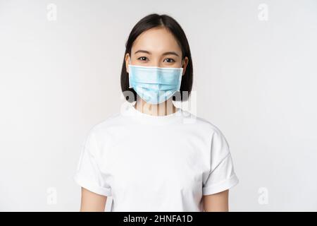 Concept de santé et de pandémie de covid. Fille asiatique souriante portant un masque médical, elle a l'air heureuse et confiante, se protégeant du coronavirus Banque D'Images