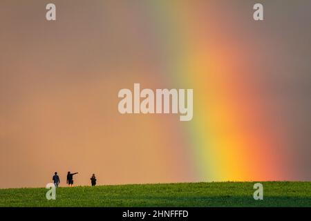 Paysage juste après une pluie, arc-en-ciel coloré sur une prairie herbacée avec de jeunes gens sur une promenade. Banque D'Images