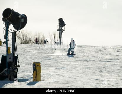 La snowboardeuse passe entre deux pistolets de ventilation inactifs (fabrication de neige) sur la partie inférieure d'une pente à la station de ski Crotched Mountain à Bennington, New Hampshire, États-Unis. Banque D'Images