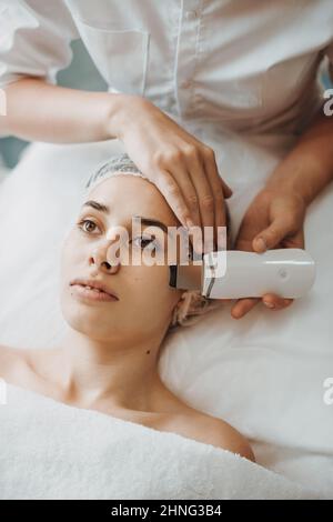 Le visage d'une femme reçoit un nettoyage ultrasonique du visage des mains d'un cosmetologue professionnel. Soin du visage. Visage de beauté. Dermatologie, cosmétologie Banque D'Images